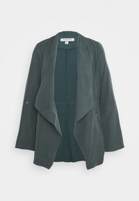 Chaqueta verde, ligera, con un frente drapeado, mangas largas, un bolsillo con cremallera y una textura suave. Presenta un diseño simple y moderno.