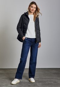 Svart vadderad jacka med huva, vit fleece-tröja och vida blå denimjeans. Modellen bär vita sneakers. Texturerade material är synliga.
