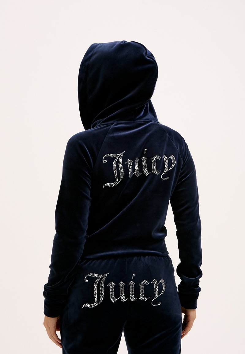 Tuta in velluto blu navy con cappuccio, con "Juicy" in strass sul retro della giacca e dei pantaloni. Tessuto morbido e design aderente.