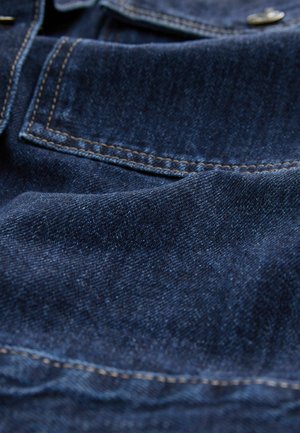 Tume sinine denim kangas, millel on nähtav tekstuur, kontrastne kollane õmblus ja tasku detail. Sile pind kerge läikega.