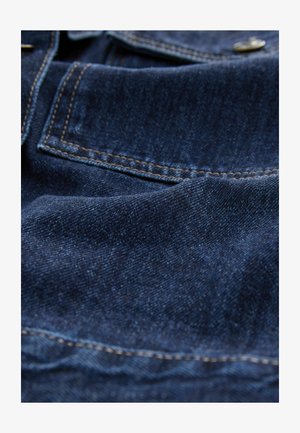 Dark blue denim fabric with visible texture, contrasting yellow stitching, and a pocket detail. Smooth surface with slight sheen.