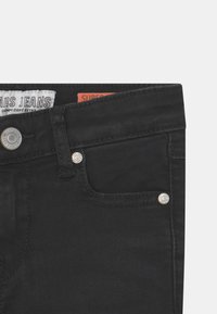 Sorte denimjeans med høy midje, utstyrt med sølvfarget hardware, sømmede lommer og en etikett som leser "Cars Jeans" på midjebåndet.