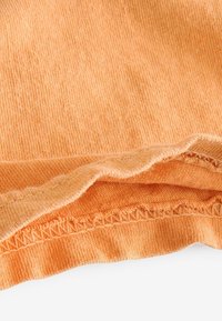 Oranger Baumwollstoff mit weicher Textur, der einen leicht gerafften Saum und ein dekoratives Stichmuster entlang des Randes aufweist.