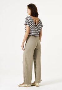 Zacht zittende grijze broek gecombineerd met een zwart-witte top met patroon, die een scoop rug en een strikdetail heeft. Gouden instappers.