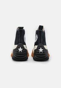 Zapatillas altas negras con suela de goma texturizada, que cuentan con un acento de estrella blanca en el talón y un logo redondo en el tobillo.