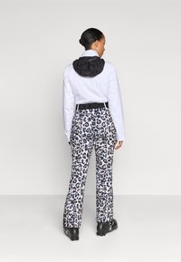 Jachetă albă cu glugă neagră, asociată cu pantaloni cu model leopard. Pantalonii au un brâu negru cu marca și un croi slim.
