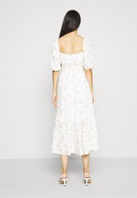 Vestido blanco con estampado floral, mangas abullonadas, espalda cuadrada y falda en capas. Presenta una cintura entallada y un delicado patrón de flores en tonos pastel.