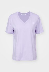 Lavendel bomull V-ringad t-shirt med korta ärmar, med en liten broderad logotyp på bröstet. Slät textur, avslappnad passform.