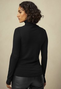 Zwarte coltrui met lange mouwen, gemaakt van een zachte, gestructureerde stof, die goed aansluit rond de torso, met smalle mouwen en een gevormde halslijn.