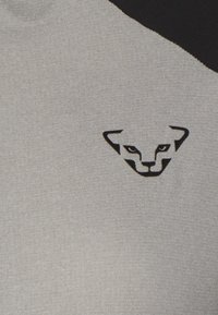 Svijetlosivi materijal s teksturiranom površinom, sa crnim detaljem na ramenu i crnim logotipom stilizirane panterske face.
