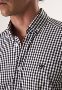 Zwart-wit geblokte overhemd met button-down kraag, voorzien van een klein geborduurd vogellogo op de borst, van katoenmateriaal.