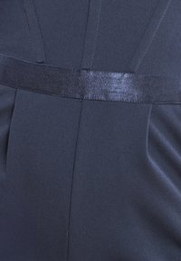 Primo piano di un tessuto blu navy scuro con una cintura in satin nera lucida e dettagli di cuciture verticali.