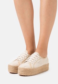 Chaussures à plateforme beige avec une tige en toile texturée et une semelle intermédiaire en jute tissé. Présentent des lacets blancs et des coutures contrastées.