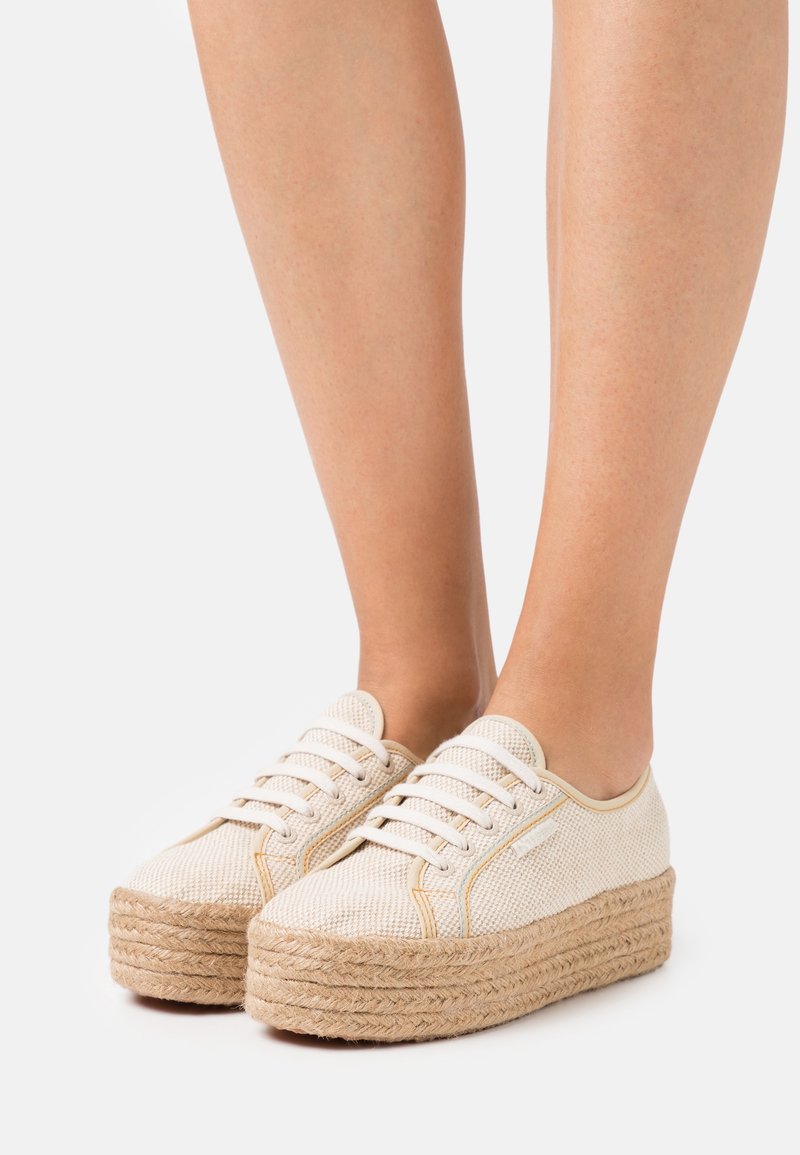 Chaussures à plateforme beige avec une tige en toile texturée et une semelle intermédiaire en jute tissé. Présentent des lacets blancs et des coutures contrastées.