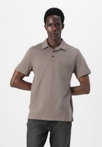 Polo à manches courtes en taupe, présentant un tissu texturé, un col, une patte de boutonnage à trois boutons et une poche poitrine.