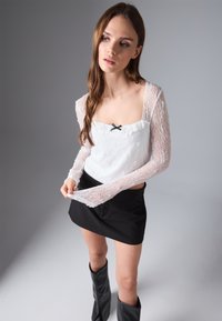 Witte kanten top met lange mouwen en een vierkante halslijn, voorzien van zwarte lintdetails, gecombineerd met een zwarte mini-jurk en kniehoogte laarzen.