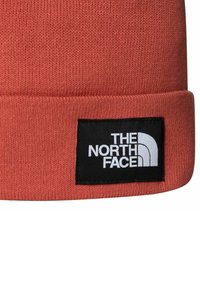 Berretto lavorato a maglia di colore corallo con risvolto. Presenta una patch rettangolare nera con testo e logo bianchi, realizzato in materiale morbido.