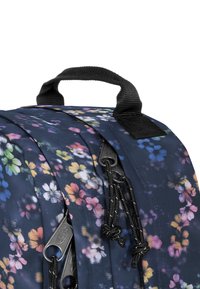 Sac à dos à motif floral bleu marine, avec des fleurs multicolores, des fermetures éclair noires et un tissu texturé avec une poignée supérieure.