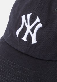 Gorra de béisbol negra con un logo bordado en blanco "NY" en la parte frontal, que presenta una tela texturizada y un diseño de visera curvada.