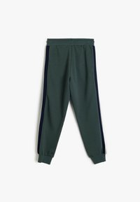 Groene joggers gemaakt van zachte stof, met marineblauwe zijstrepen en elastische manchetten voor een strakke pasvorm rond de enkels.