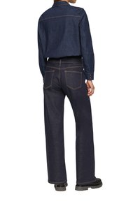 Ciemnoniebieska koszula wykonana z denimu o prostym kroju, z detalem w postaci karczku z tyłu i zapięciem na guziki; zestawiona z szerokimi ciemnymi dżinsami z tylnymi kieszeniami i kontrastowym przeszyciem.