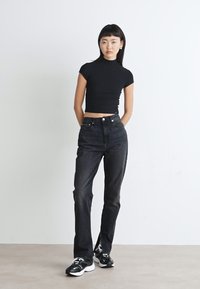 Svart, riflet crop top kombinert med høyreiste, mørke denimjeans. Modellen har på seg svarte og hvite joggesko. Enkelt design med minimale detaljer.