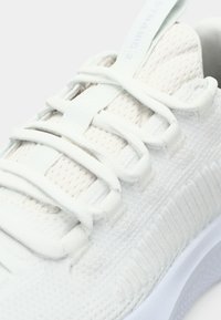 Lightweight white athletic sneaker with mesh upper, flat laces, ribbed texture on the side, and padded collar for comfort.