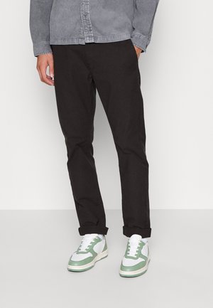 Black slim-fit pants paired with white and green sneakers. The shoes have a leather upper with green accents and a white sole.