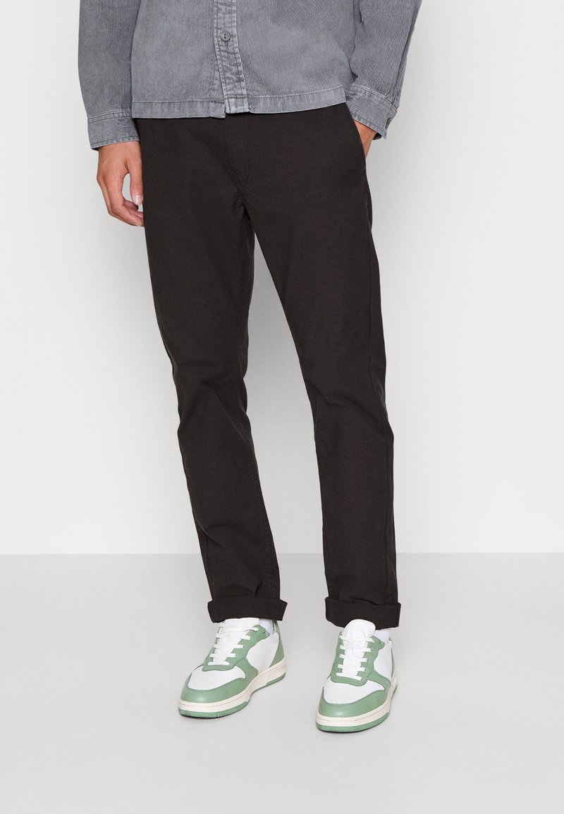 Pantaloni negri skinny asortați cu adidași albi și verzi. Pantofii au un superior din piele cu accente verzi și o talpă albă.