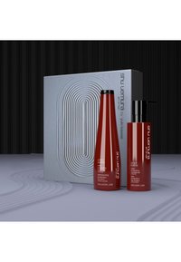 Czerwone butelki szamponu i odżywki o eleganckim wyglądzie, oznaczone napisem "color lustre". Towarzyszy im teksturowane szare pudełko z okrągłym wzorem.