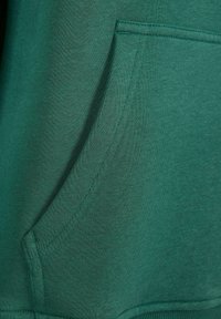 Tessuto di felpa verde con una texture liscia; presenta una tasca frontale, dettagli di cucitura e un design classico della tasca a marsupio.