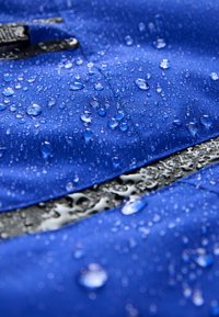 Tissu imperméable bleu avec de nombreuses gouttes d'eau perlées à la surface, mettant en valeur la résistance à l'eau et les détails de la texture.