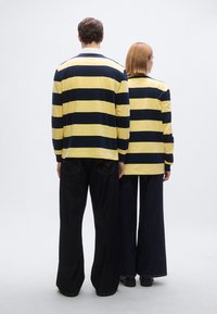 Μπλούζες με μακριά μανίκια, κίτρινες με ναυτικές ρίγες και γιακά, συνδυασμένες με παντελόνια από σκούρο τζιν με φαρδιά μπατζάκια. Και τα δύο από πίσω.