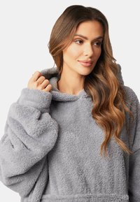 Sudadera con capucha de gran tamaño en tejido de felpa gris. Presenta una gran capucha, mangas largas y una textura suave sin patrones visibles ni herrajes.