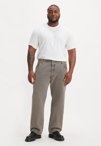 Grijze wijde jeans met een hoge taille, gecombineerd met een goed zittend wit t-shirt. Zwarte chunky schoenen en een gouden ketting als accessoires.