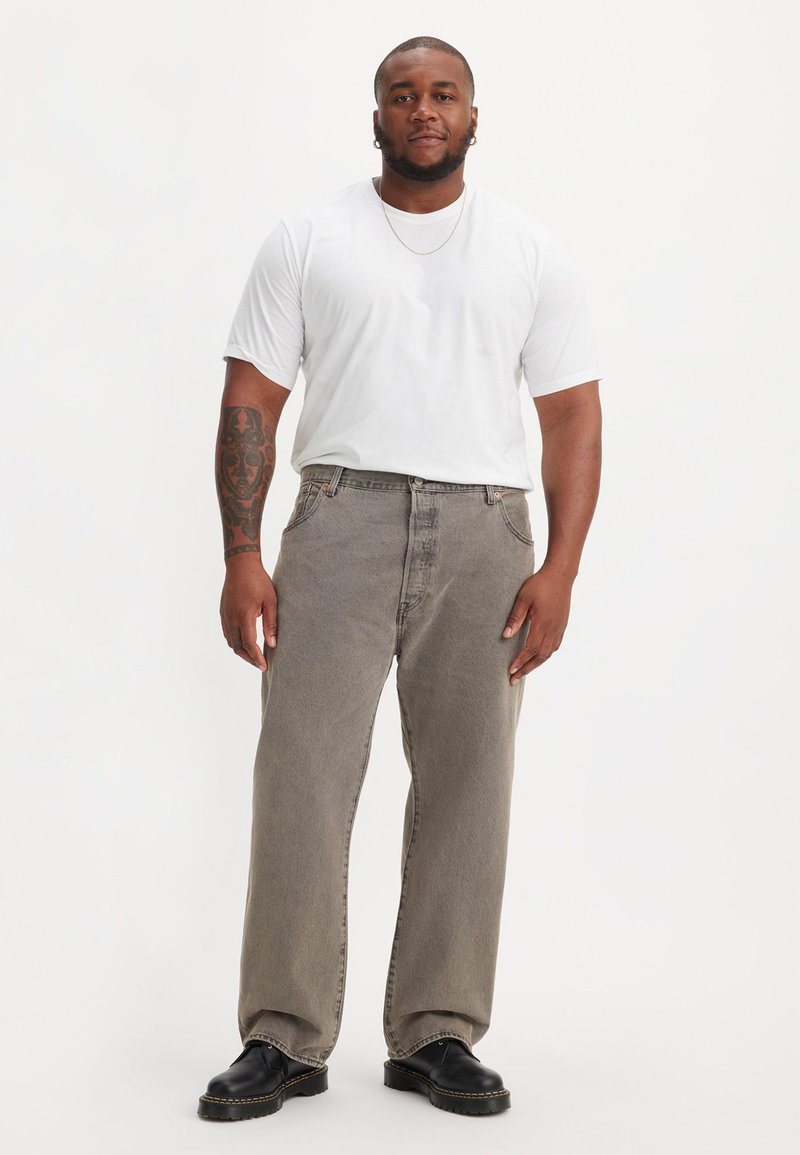 Jean large gris à taille haute, associé à un t-shirt blanc ajusté. Chaussures noires massives et chaîne en or comme accessoires.