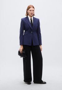 Ναυτικό σακάκι σε στενή γραμμή, με ένα κουμπί. Λευκό πουκάμισο, μαύρη γραβάτα. Μαύρο παντελόνι με φαρδιά πόδια, μαύρη τσάντα και λαμπερά μαύρα παπούτσια.