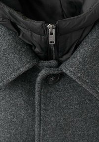 Abrigo de mezcla de lana gris con un forro interno negro acolchado, gran cuello y un cierre frontal con cremallera y tirador plateado, además de un botón de cierre.