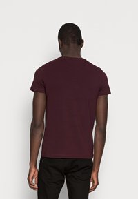 Mørk burgunder kortærmet T-shirt med rund hals, der har en tætsiddende pasform og blødt bomuldsstof, set fra bagsiden.