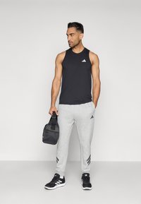 Svart ärmlös idrottstopp, grå joggingbyxor med tre randmönster, svarta sportskor och en mörk gymväska. En enkel träningsoutfit.