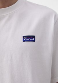T-shirt de algodão branco com um retângulo azul marinho apresentando o logótipo "Penfield" em branco e gráficos de montanha vermelhos. Design clássico de gola redonda.