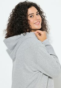 Harmaa huppari, jossa pehmeä pinta, istuva malli ja huppu. Vaatteessa on kaartuvat saumat ja rento leikkaus, jotka lisäävät mukavuutta.