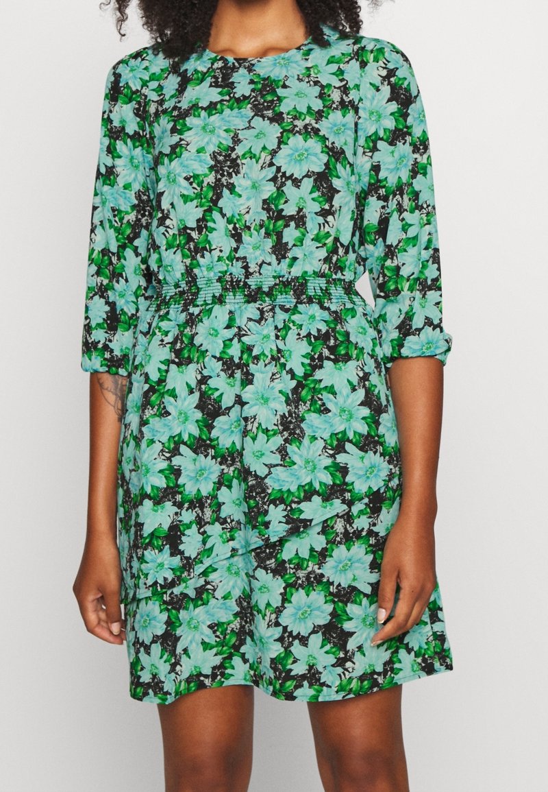 Vestido floral con un fondo negro y grandes flores en verde menta y teal. Tiene mangas de tres cuartos y una cinturilla elástica.