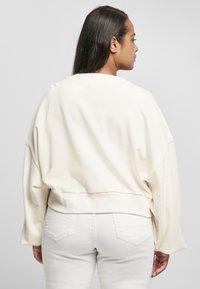 Crème cropped sweatshirt met verlaagde schouders, brede mouwen en een ribbelrand, gecombineerd met witte aansluitende jeans. Zachte textuur, minimalistisch ontwerp.