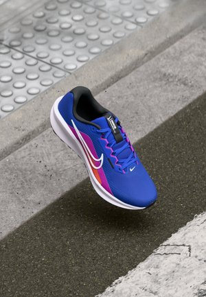 Scarpa sportiva blu con tomaia in mesh, con accenti viola e arancioni, logo swoosh bianco e collo imbottito nero. Suola bianca con grip testurizzato.