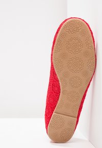 Scarpa da balletto piatta in pizzo rosso, suola rivolta verso la fotocamera con un motivo floreale, misura 37, appoggiata contro uno sfondo angolare bianco.