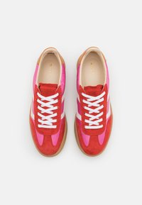 Rote und rosa Wildledersneaker mit weißen Schnürsenkeln, ausgestattet mit einer hellbraunen Lederferse und einer Sohle aus Gummi. Klassisches sportliches Design.
