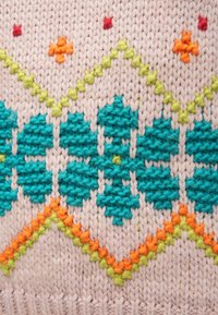 Textil de punto con base rosa claro, flores en color verde azulado, estrellas naranjas y patrones de zigzag verdes; textura suave con apariencia de hilo grueso.