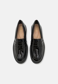 Schwarze Lackleder-Slipper mit runder Zehenform und dekorativem Riemen über dem Spann. Ausgestattet mit einer gepolsterten Innensohle für hohen Komfort.