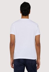 Biała bawełniana koszulka z klasycznym okrągłym dekoltem i krótkimi rękawami, o prostej, gładkiej fakturze i prostym kroju dołu.